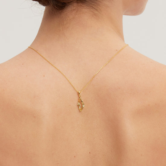 Gold necklace with a pendant on a person's neck against a neutral background