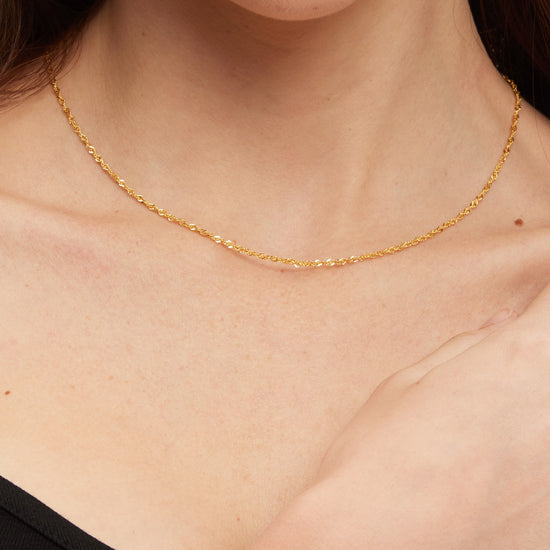 Gold necklace on a person's neck with a plain background