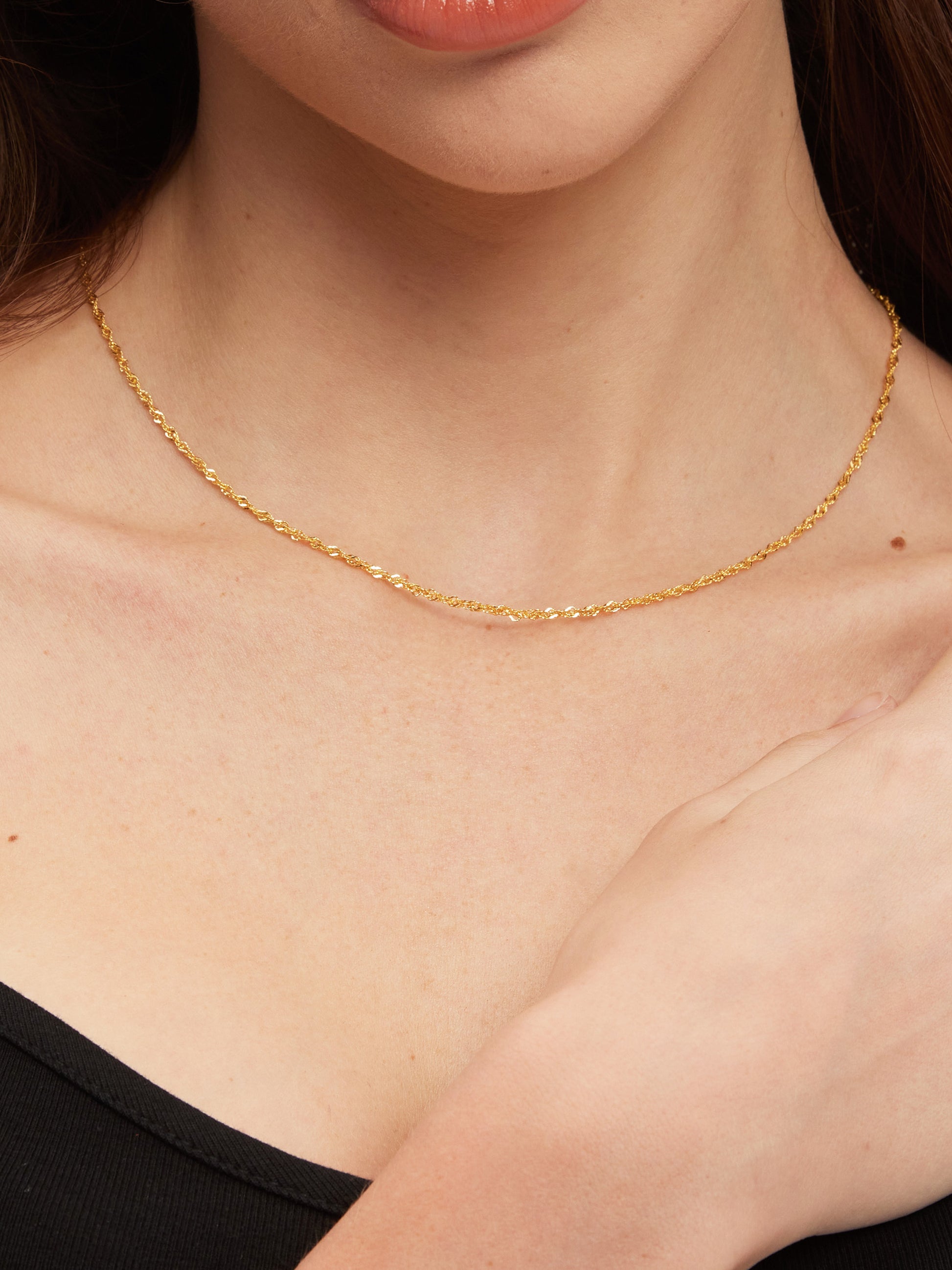 Gold necklace on a person's neck with a plain background