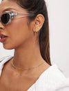 Woman wearing clear sunglasses, gold hoop earrings, and a gold chain necklace on a white background