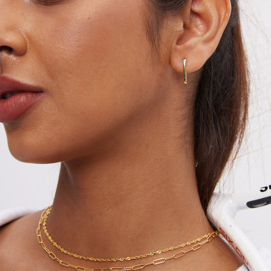 Close-up of a woman wearing gold hoop earrings, clip-like chain, and twist rope chain