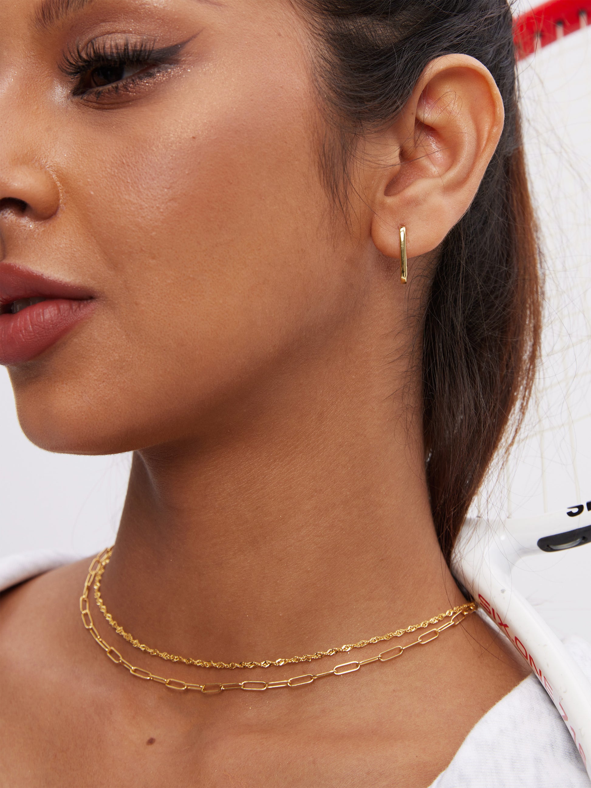 Close-up of a woman wearing gold hoop earrings, clip-like chain, and twist rope chain