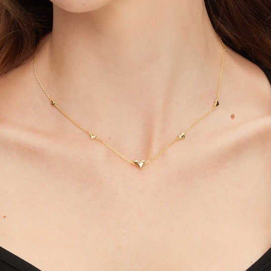 Gold necklace with small heart pendants on a person wearing a black top.