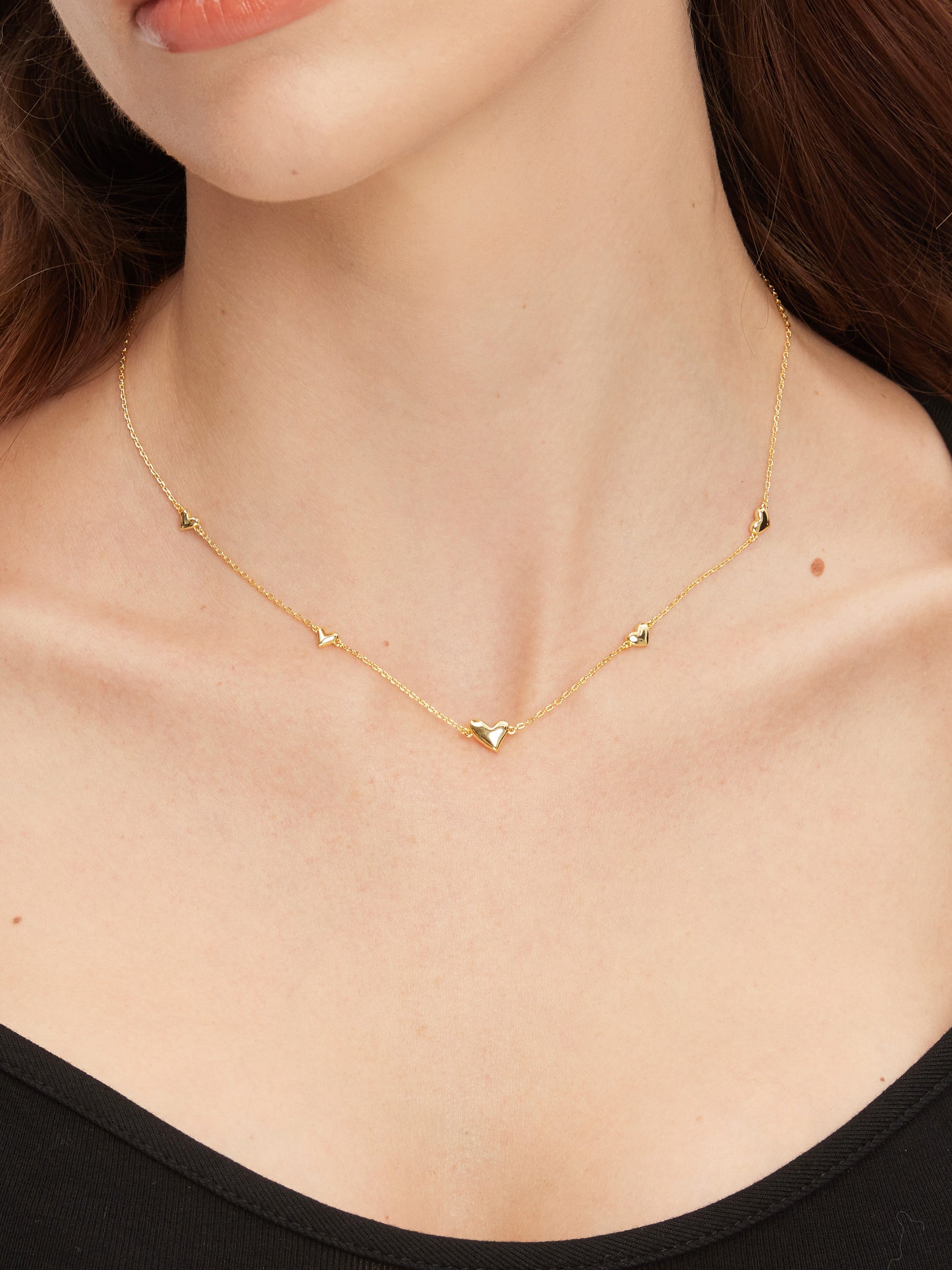 Gold necklace with small heart pendants on a person wearing a black top.