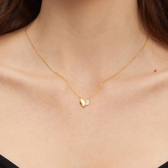 Gold necklace with a heart-like pendant on a person wearing a black top.