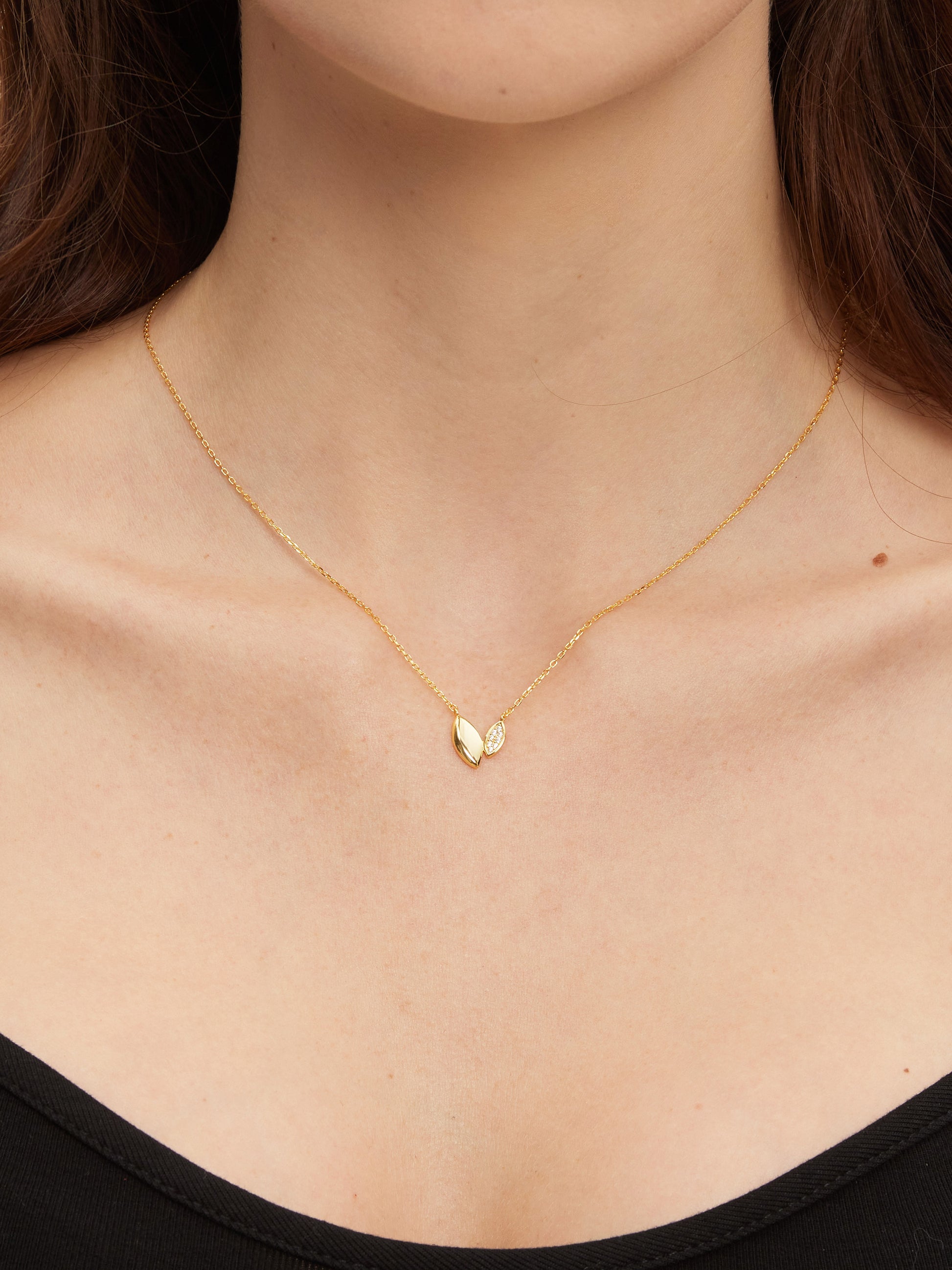 Gold necklace with a heart-like pendant on a person wearing a black top.