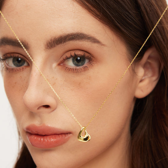 Close-up of a woman wearing a gold necklace with a teardrop pendant.