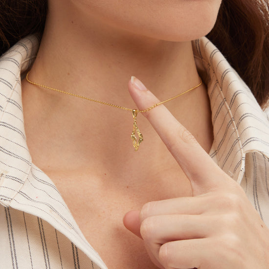 Gold necklace with a pendant worn by a person, pointing to it.