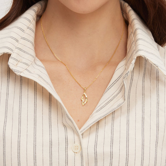 Close-up of a person wearing a gold necklace with a pendant against a neutral background