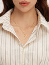 Close-up of a person wearing a gold necklace with a pendant against a neutral background