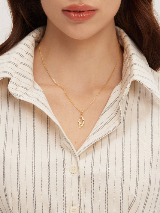 Close-up of a person wearing a gold necklace with a pendant against a neutral background