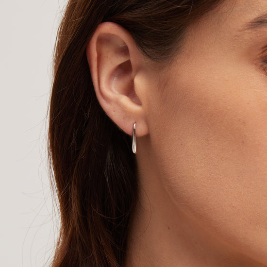 Close-up of a person wearing a silver earring on a neutral background