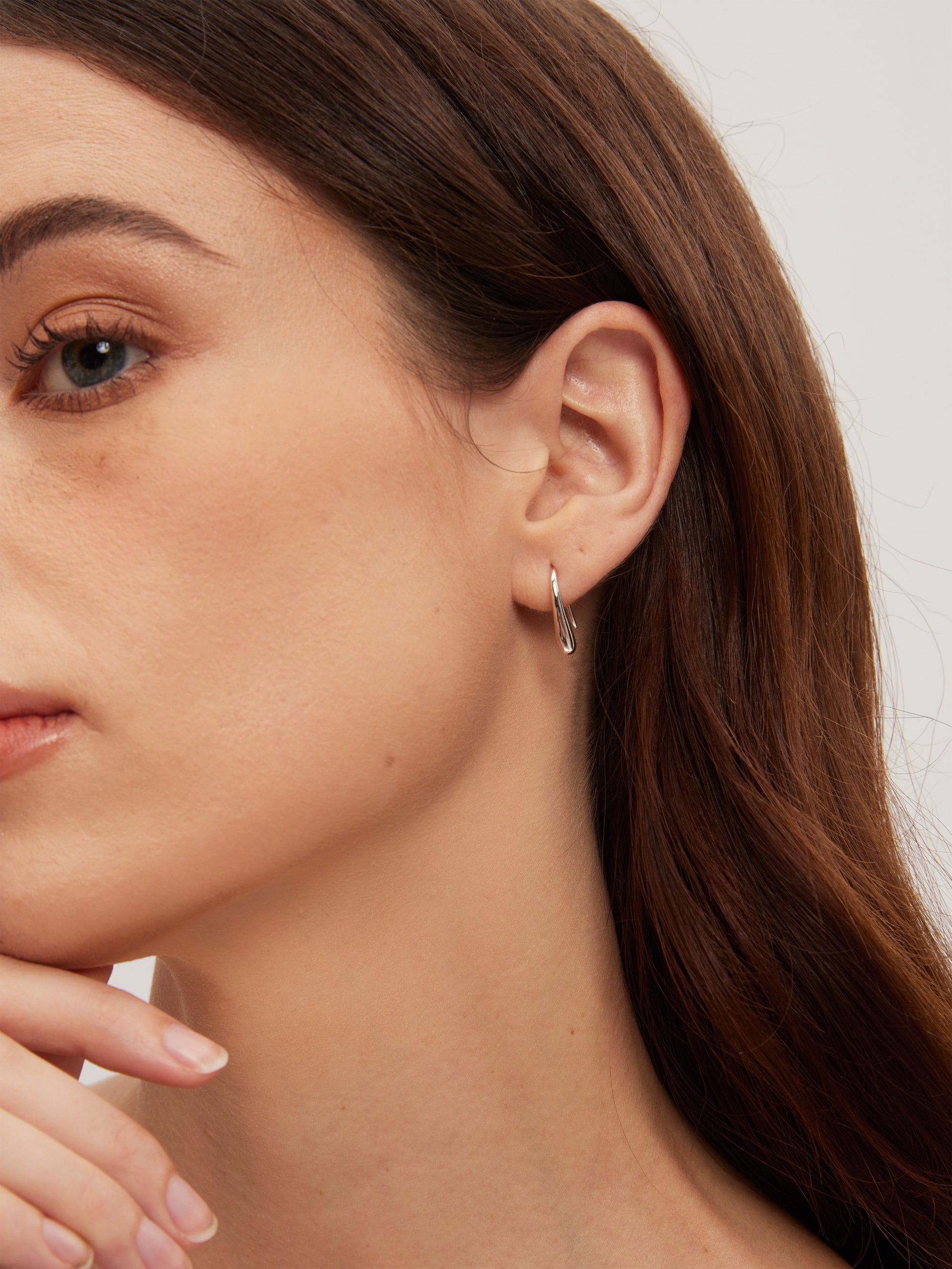 Close-up of a woman wearing a silver hoop earring with a neutral background