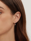 Close-up of a person wearing a silver hoop earring with a plain background