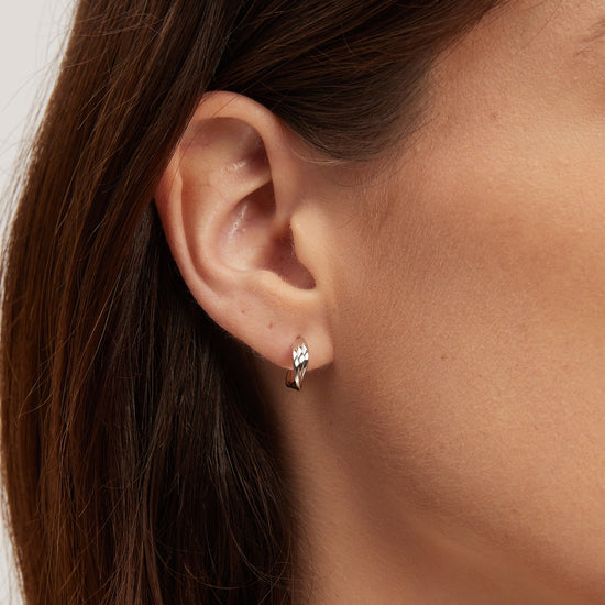 Close-up of an ear wearing a small earring with a neutral background