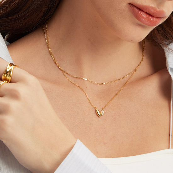 Close-up of a person wearing a gold necklace with a leaf-like pendant, layered with a gold chain