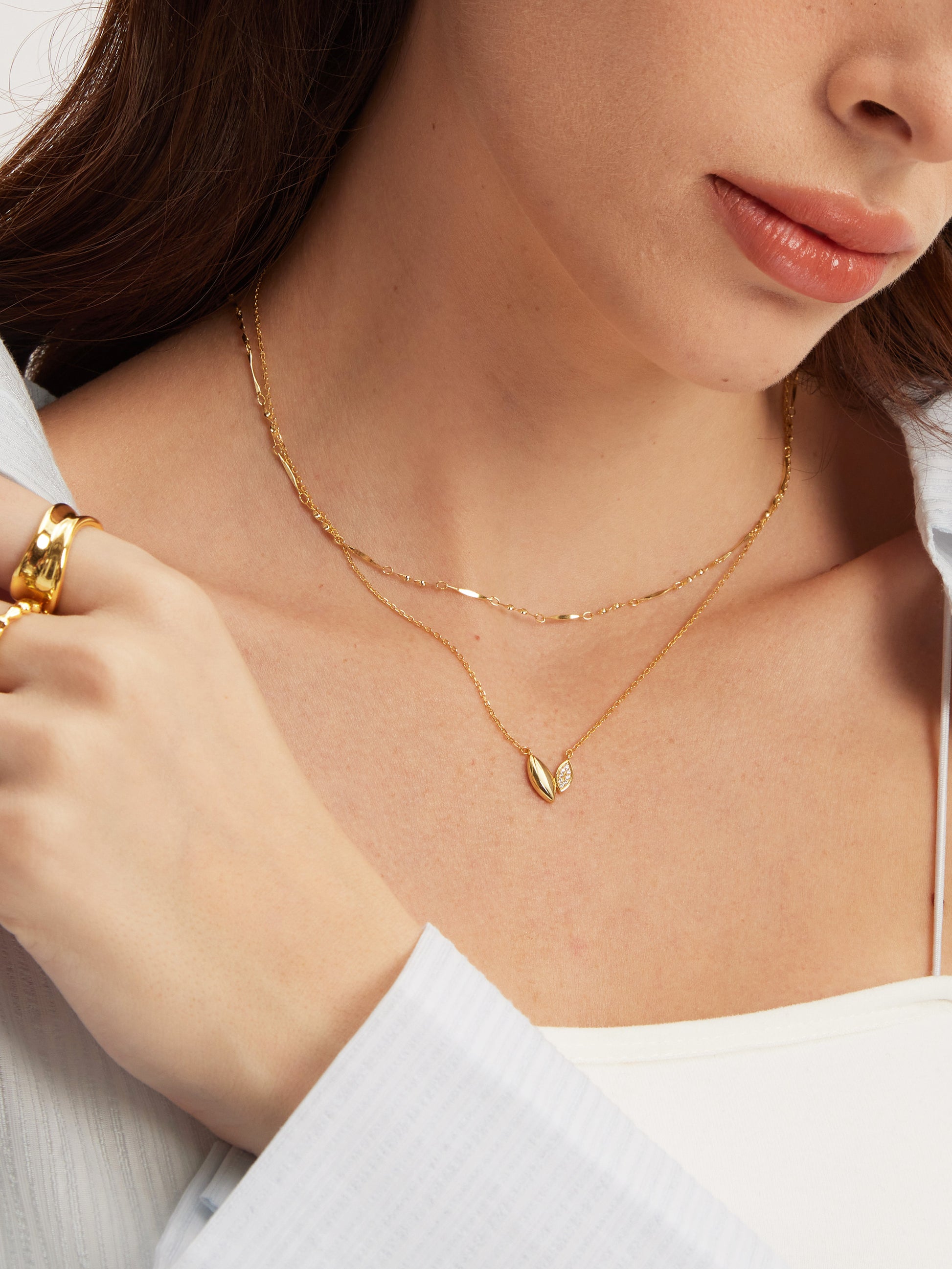 Close-up of a person wearing a gold necklace with a leaf-like pendant, layered with a gold chain