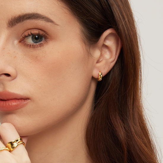 Close-up of a woman wearing gold earrings and a ring with a plain background