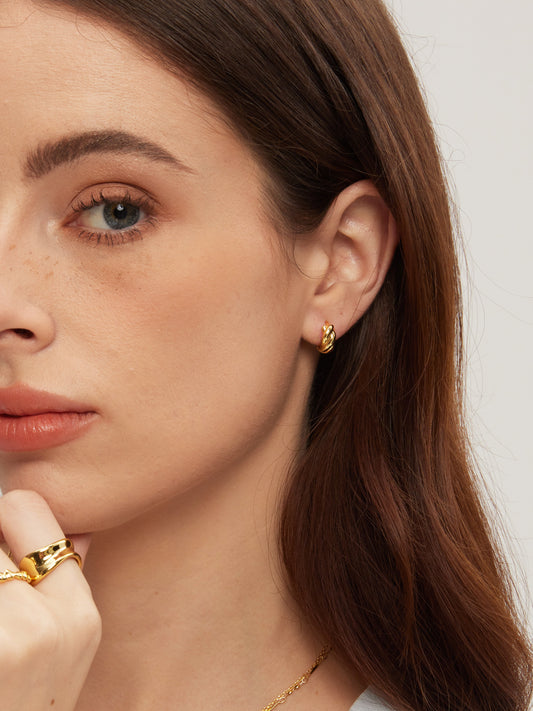 Close-up of a woman wearing gold earrings and a ring with a plain background