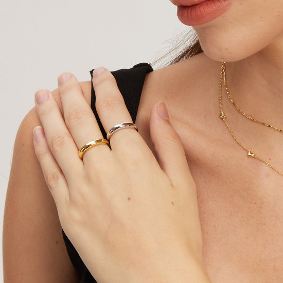 Close-up of a person wearing gold and silver classic rings and a necklace on a plain background