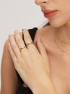 Close-up of a person wearing gold and silver classic rings and a necklace on a plain background