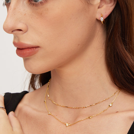Close-up of a woman wearing gold necklaces and earrings against a neutral background
