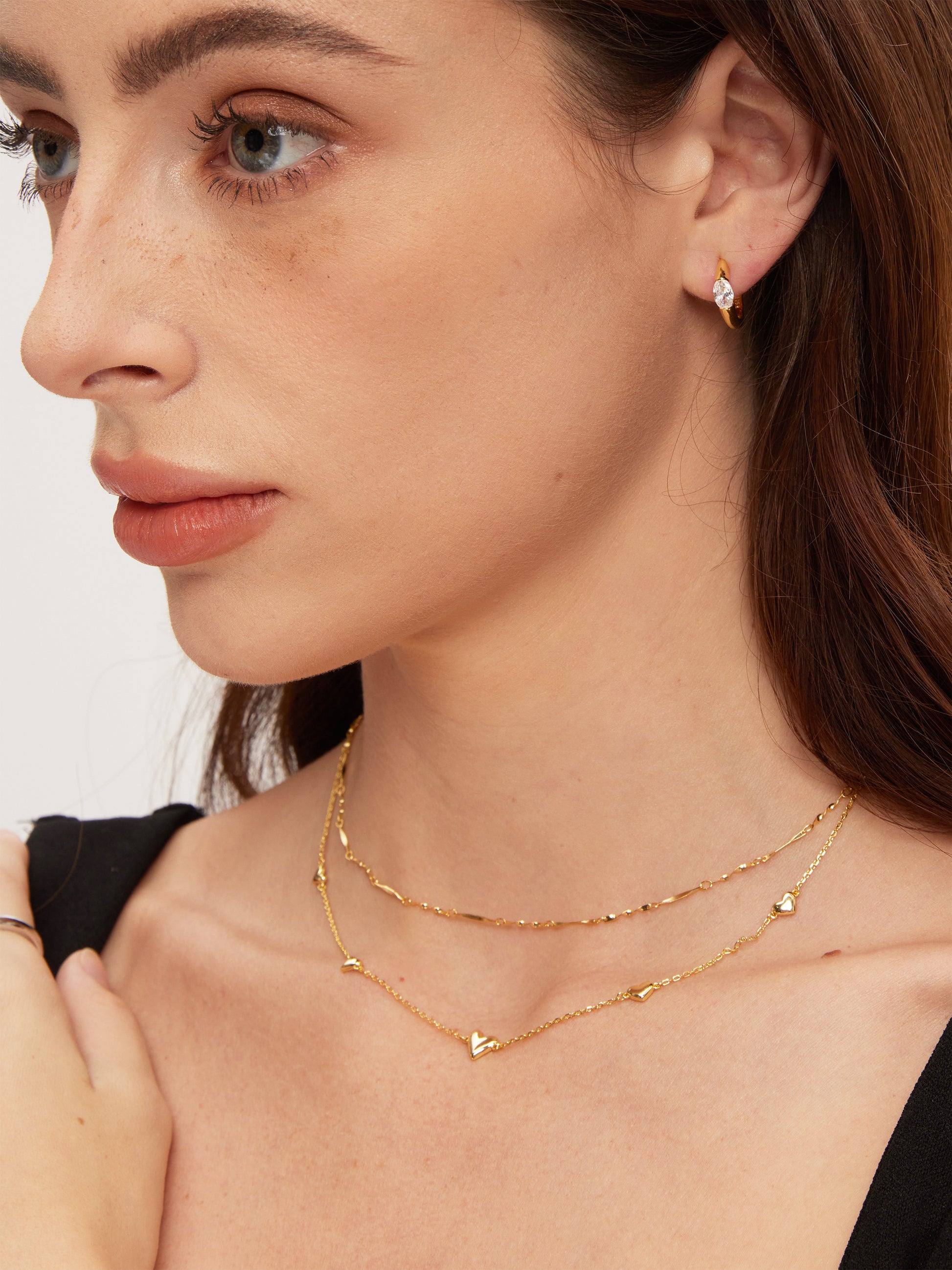 Close-up of a woman wearing gold necklaces and earrings against a neutral background