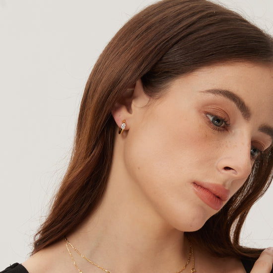 Woman wearing gold earrings and necklaces against a plain background