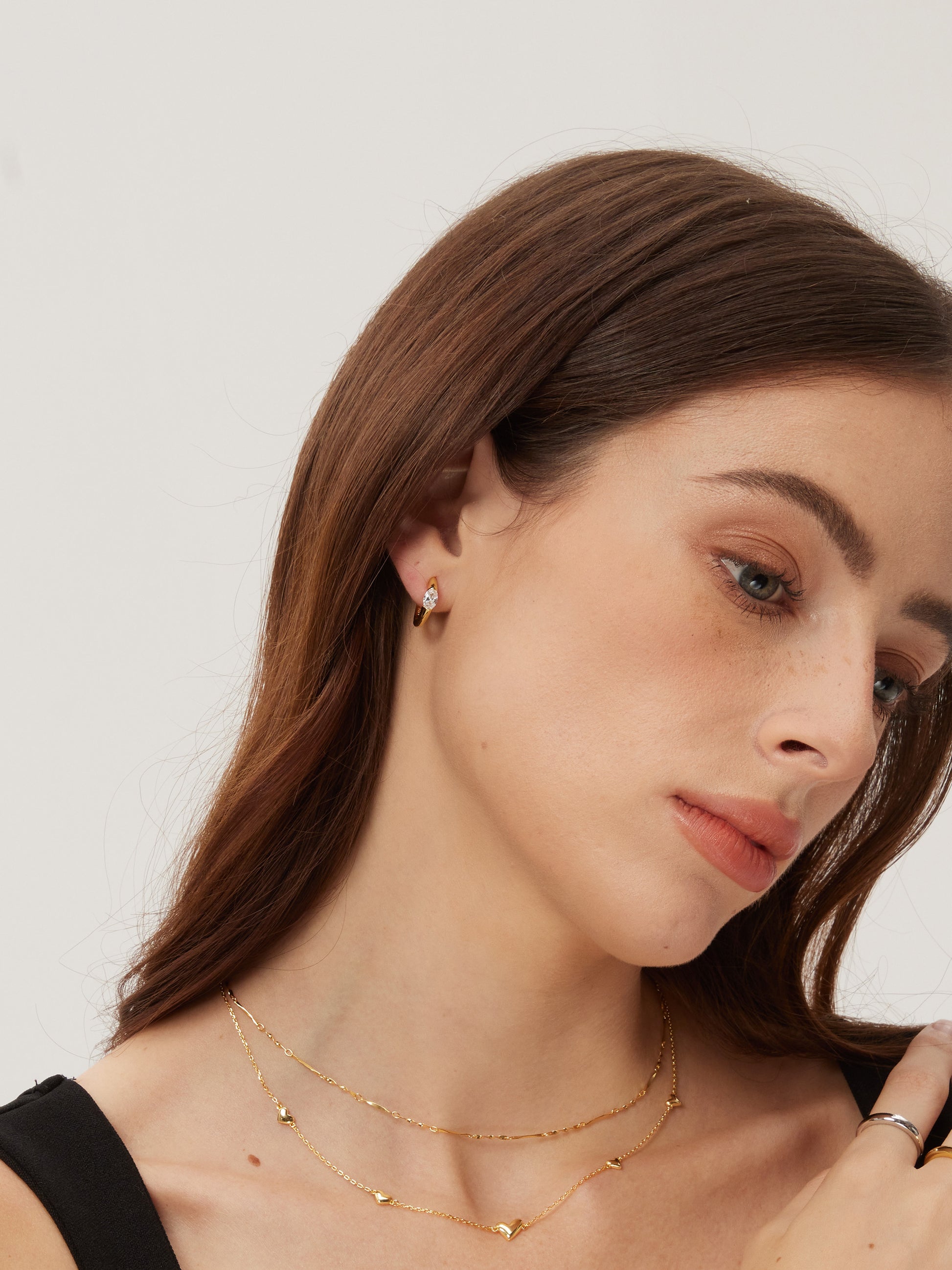 Woman wearing gold earrings and necklaces against a plain background