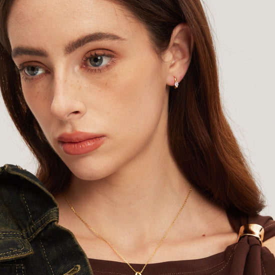 Close-up of a woman wearing a gold necklace and earrings on a plain background