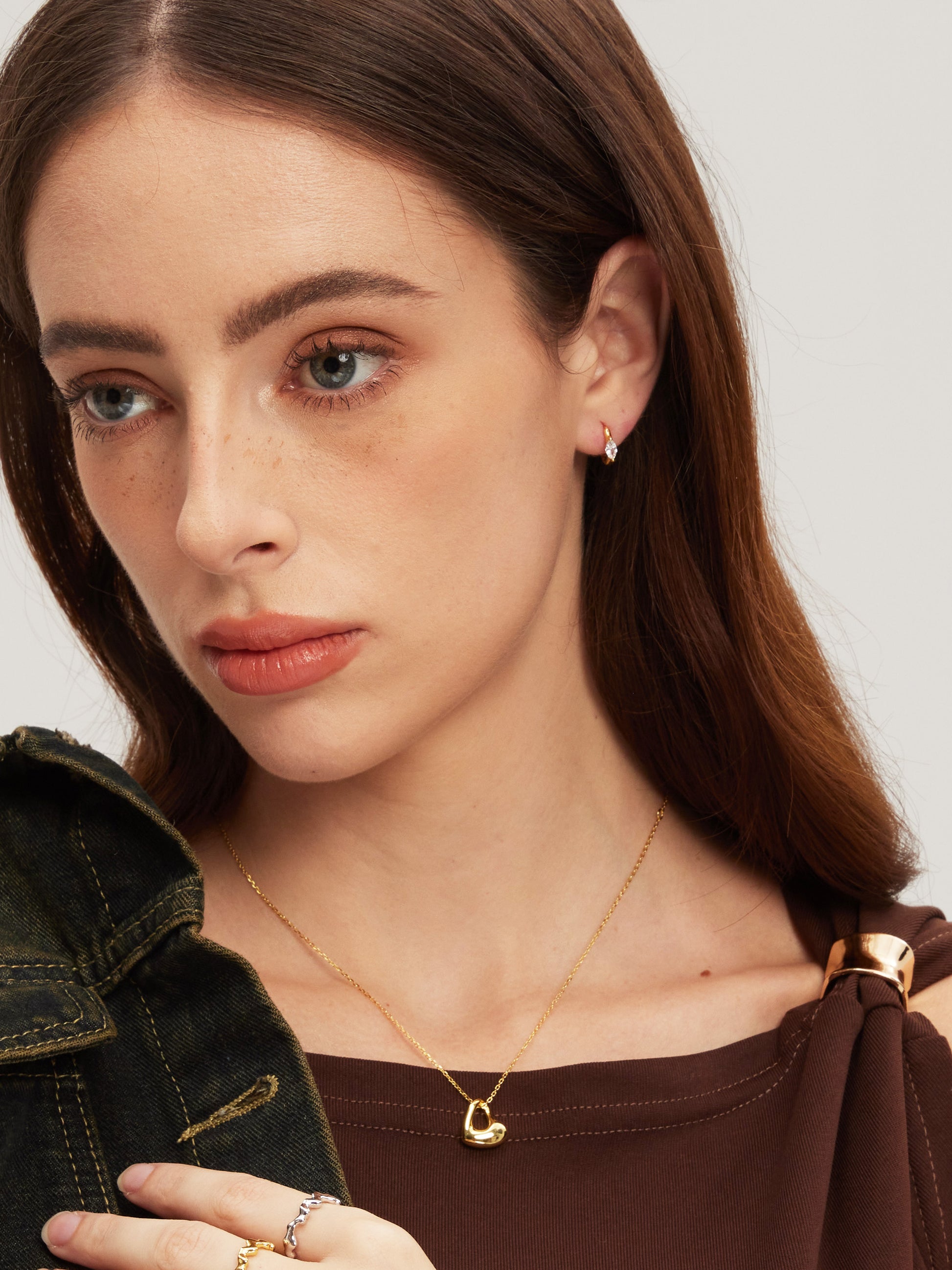 Close-up of a woman wearing a gold necklace and earrings on a plain background
