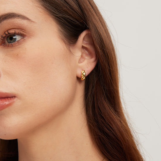 Close-up of a woman wearing gold earrings with a plain background