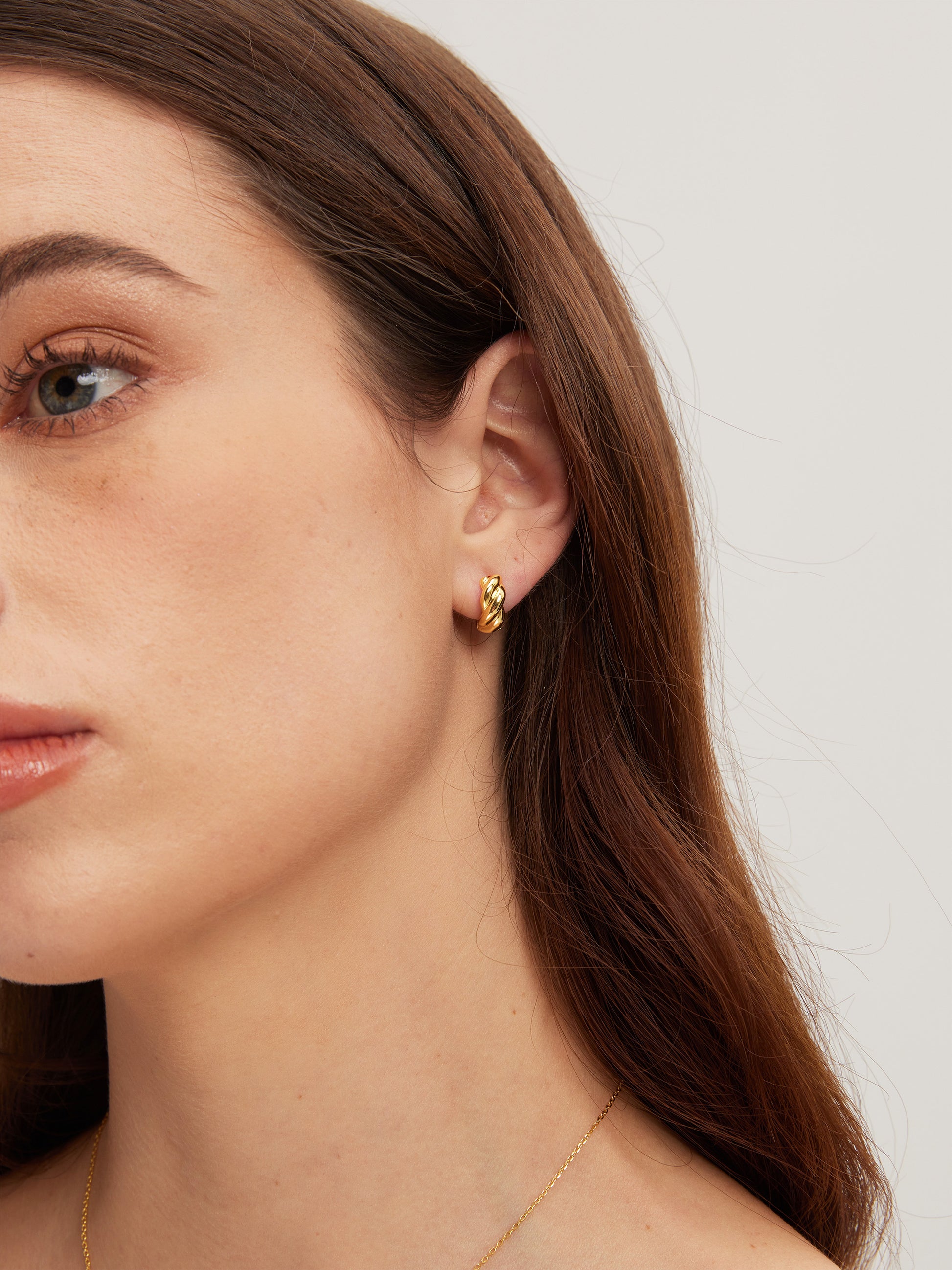 Close-up of a woman wearing gold earrings with a plain background