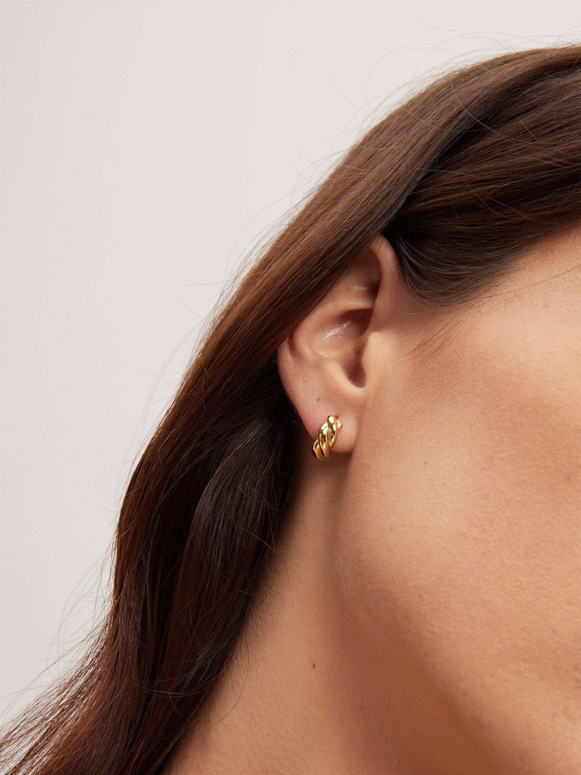 Gold earring worn by a person with a neutral background