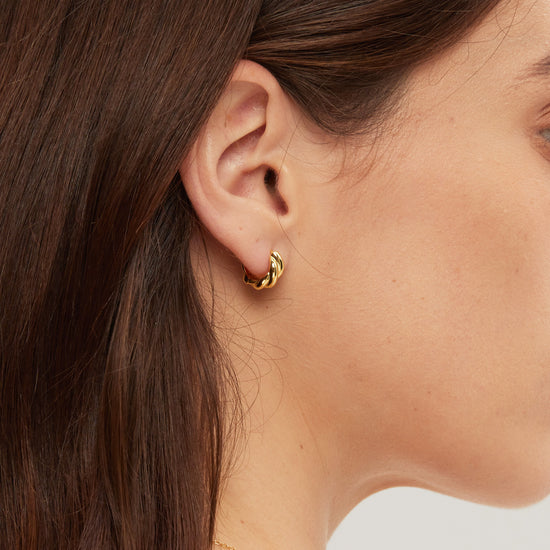 Close-up of a person wearing a gold hoop earring with a blurred background