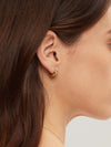 Close-up of a person wearing a gold hoop earring with a blurred background