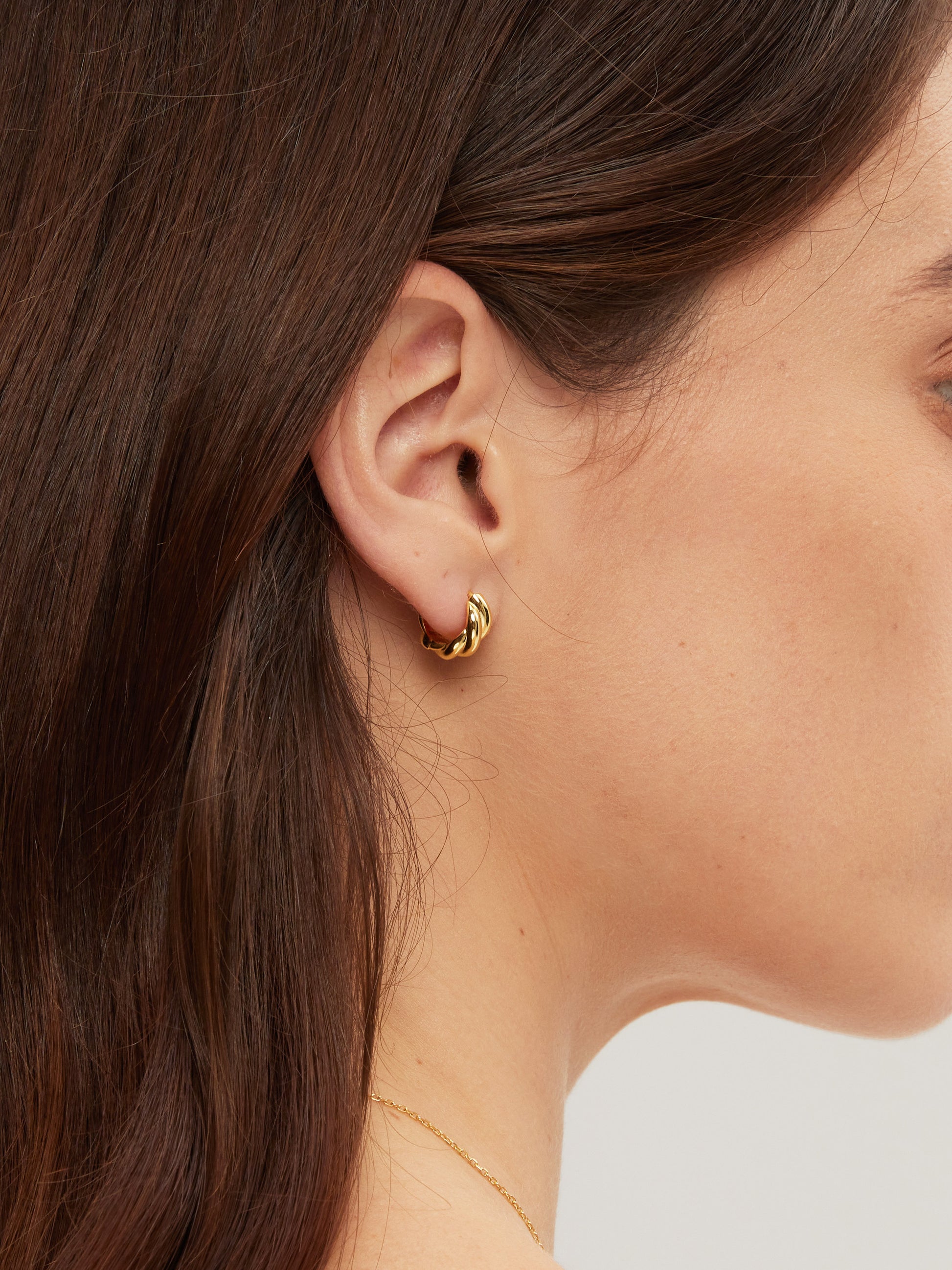 Close-up of a person wearing a gold hoop earring with a blurred background