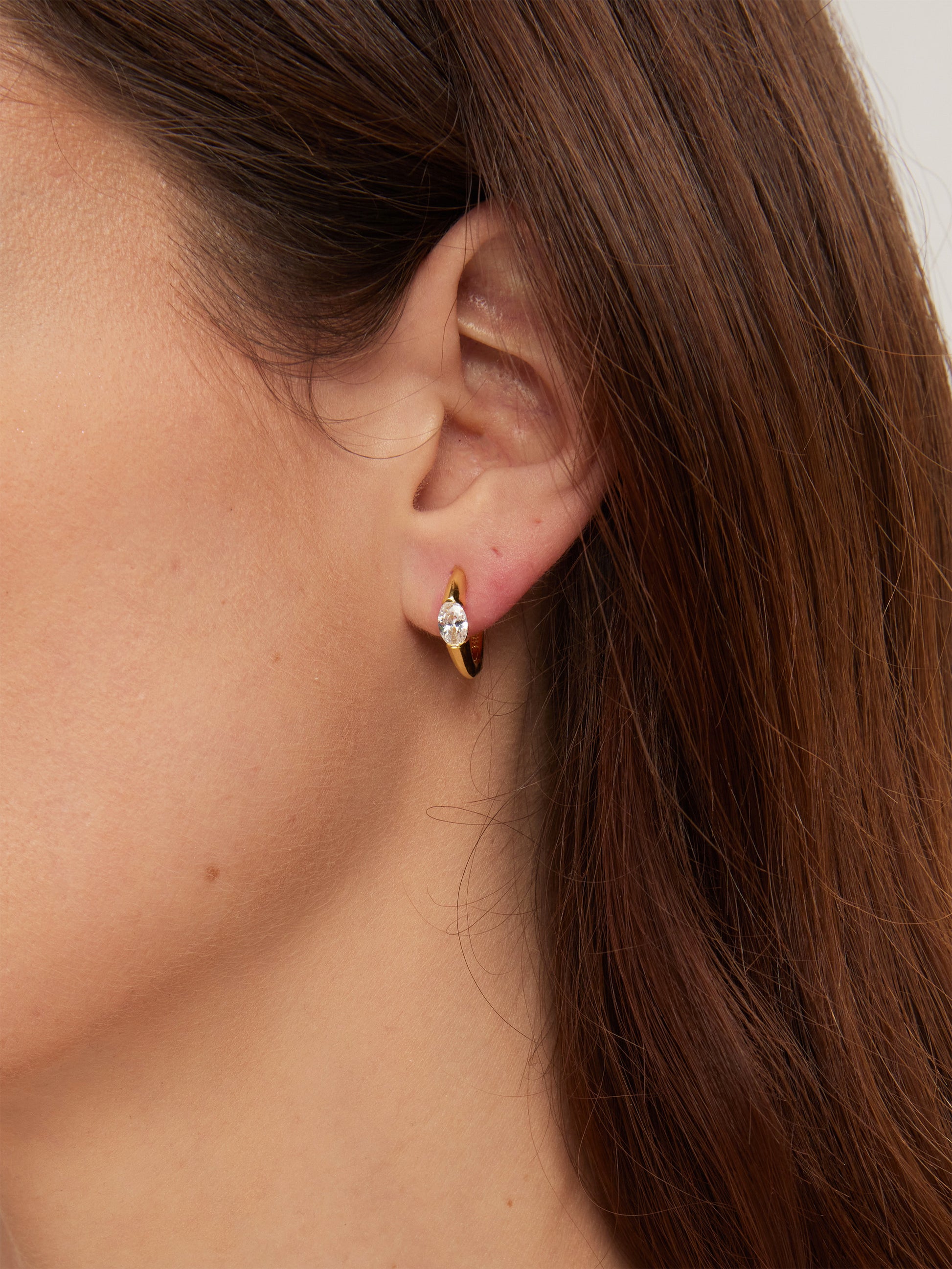 Close-up of an ear wearing a gold earring with a clear gemstone.