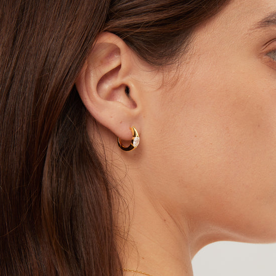 Close-up of a person wearing a gold hoop earring with a blurred background