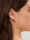 Close-up of a person wearing a gold hoop earring with a blurred background