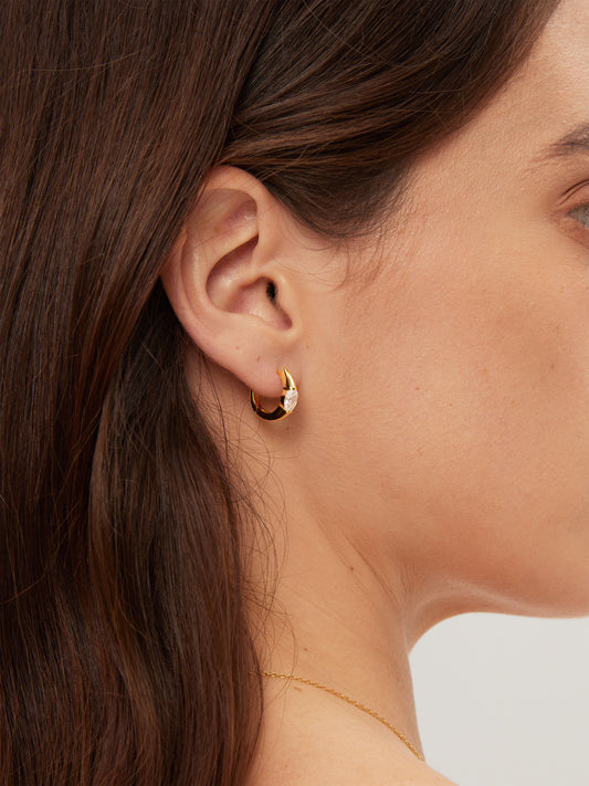 Close-up of a person wearing a gold hoop earring with a blurred background