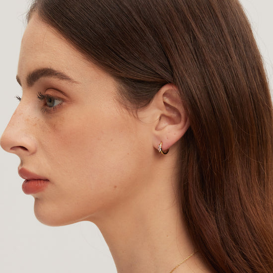 Close-up of a woman wearing a gold earring on a plain background