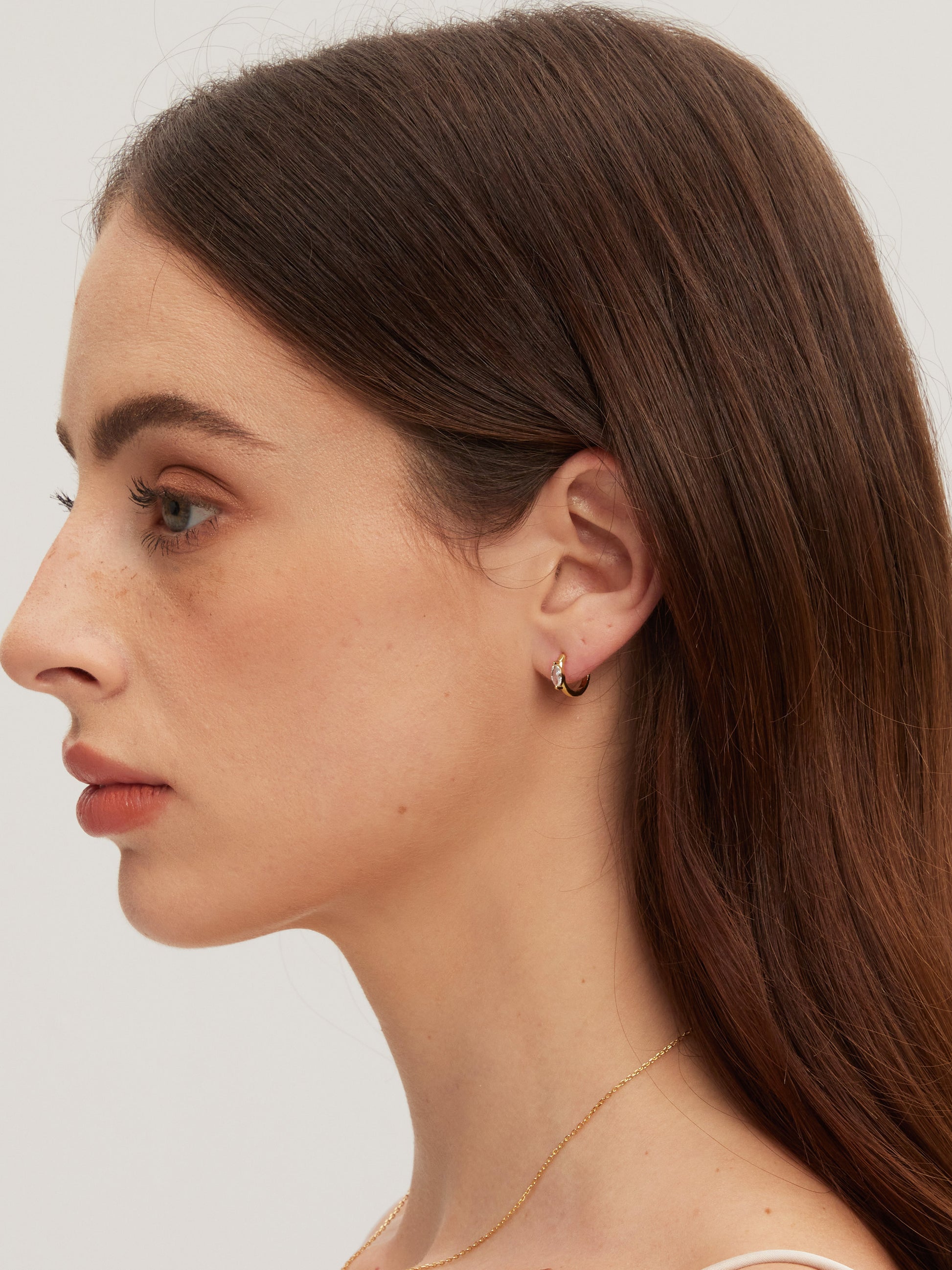 Close-up of a woman wearing a gold earring on a plain background