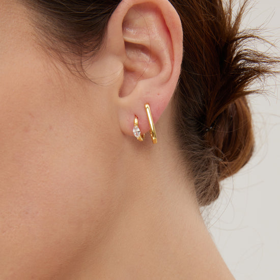 Close-up of an ear wearing gold hoops and huggies with a blurred background