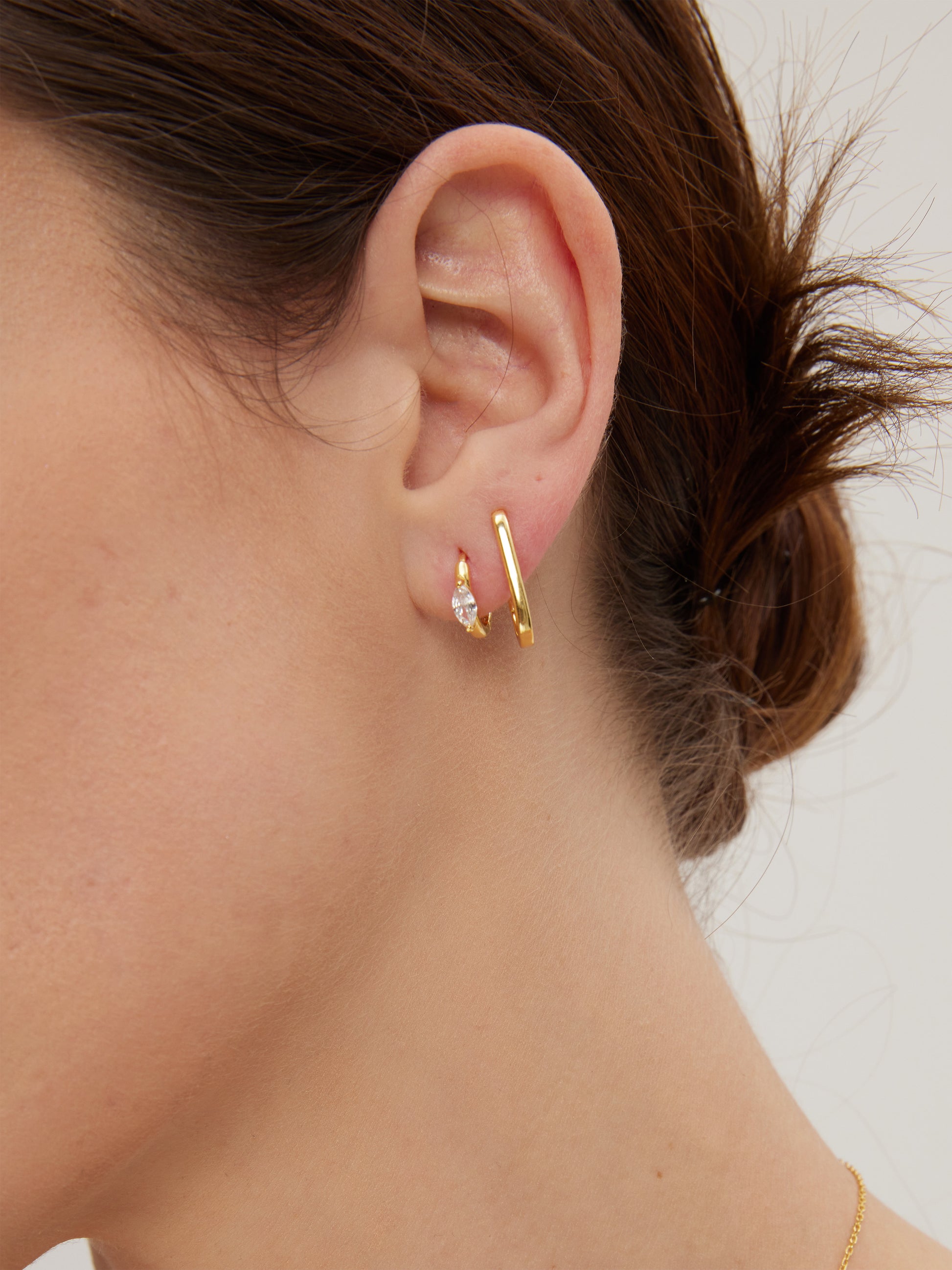 Close-up of an ear wearing gold hoops and huggies with a blurred background