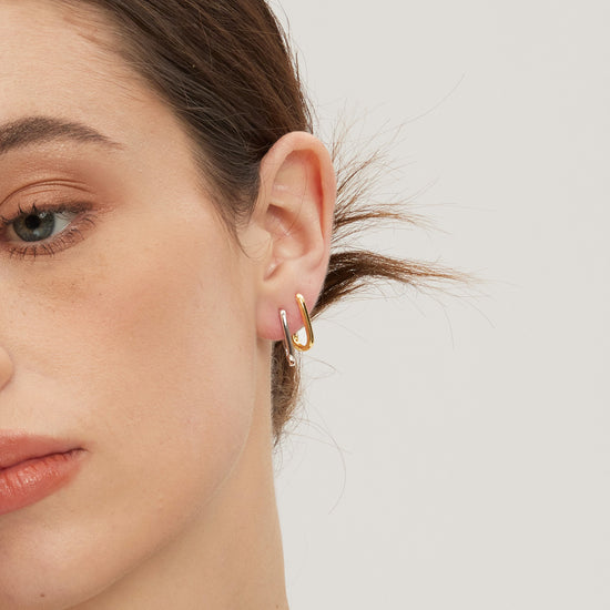 Close-up of a person wearing gold and silver huggies on a plain background