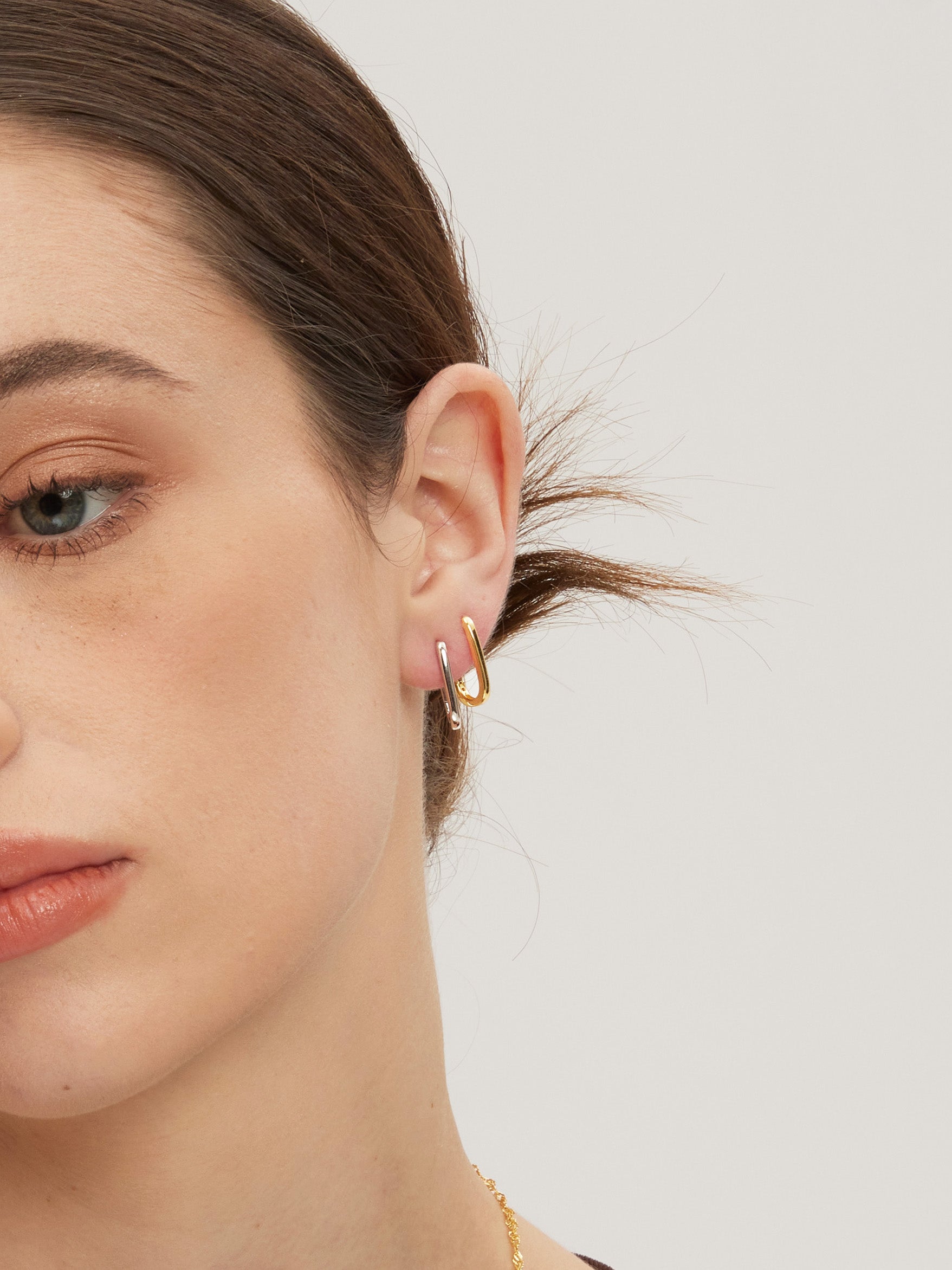 Close-up of a person wearing gold and silver huggies on a plain background