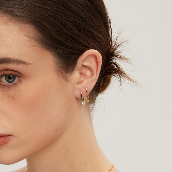Close-up of a woman wearing gold and silver huggies with a plain background