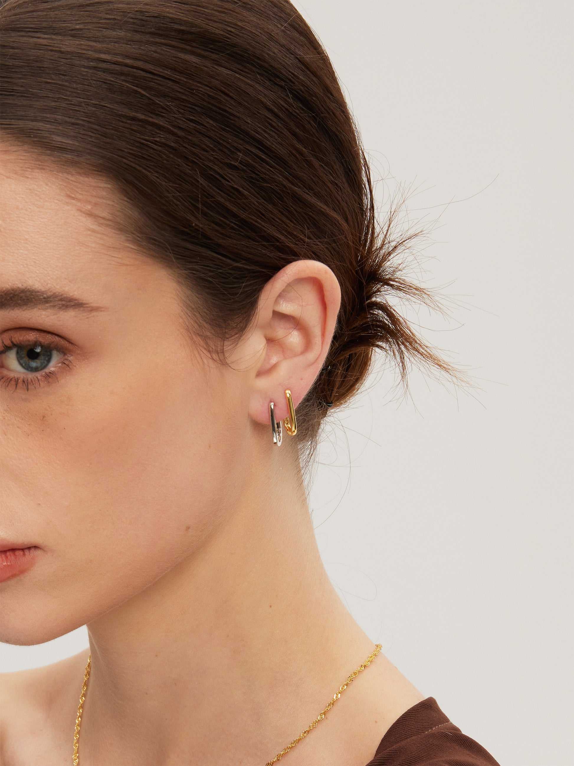 Close-up of a woman wearing gold and silver huggies with a plain background