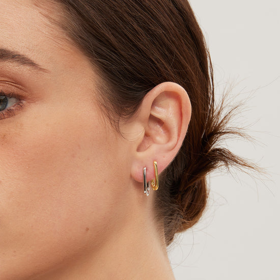Close-up of a person wearing gold and silver hoop earrings with a neutral background